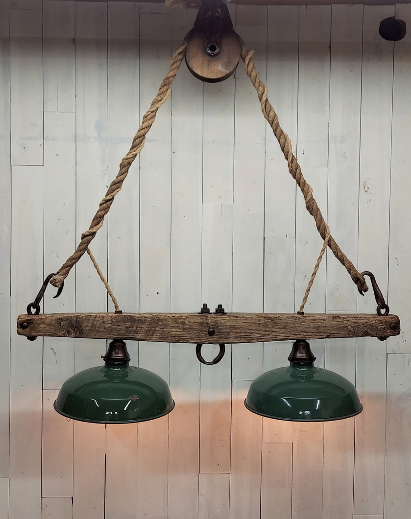 Suspended from a single wheel barn pulley by a vintage hemp rope, two barn shade with Edison lights attached to a horse yoke make up this rustic chandelier.  The barn shades display their original green paint, and timeworn patina.  Dimensions are 38 in W, 44 in H.  Lights are illuminated.