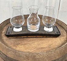 Load image into Gallery viewer, A whiskey barrel stave coaster sporting 3 indents, with a Glencairn glass at each end, and a small carafe in the middle. The coaster sits on a barrel top.