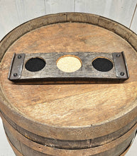 Load image into Gallery viewer, A whiskey barrel stave coaster sporting 3 indents. The two at each end are covered in felt, and the middle one in cork. There is a barrel ring fastened at each end of the coaster. The coaster sits on a barrel top.