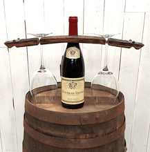 Load image into Gallery viewer, Wine bottle centered on a wooden barrel top, with a rustic barrel stave set over the bottle neck, and a stemmed wine glass hanging on each side of the bottle.