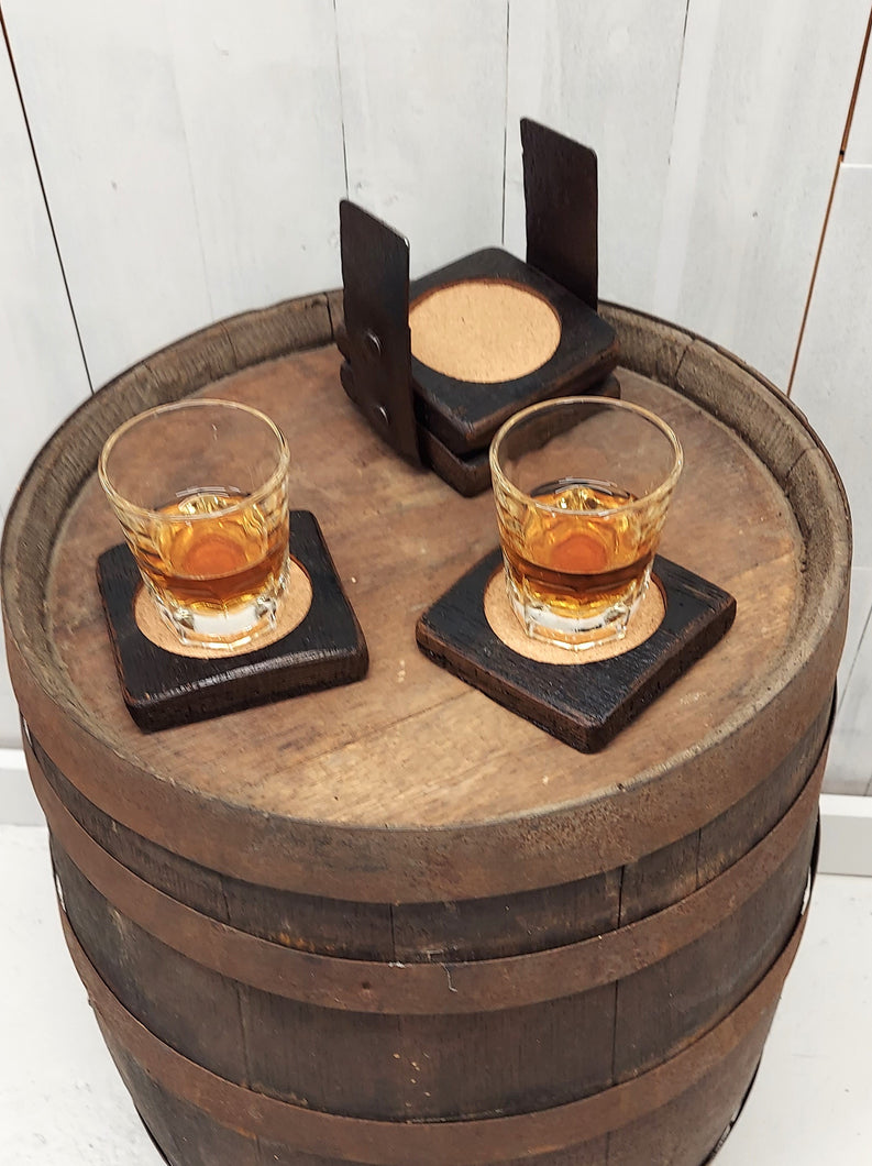 A top view of four coasters fashioned from whiskey barrel staves displaying two whiskey filled glasses on top of a rustic whiskey barrel.
