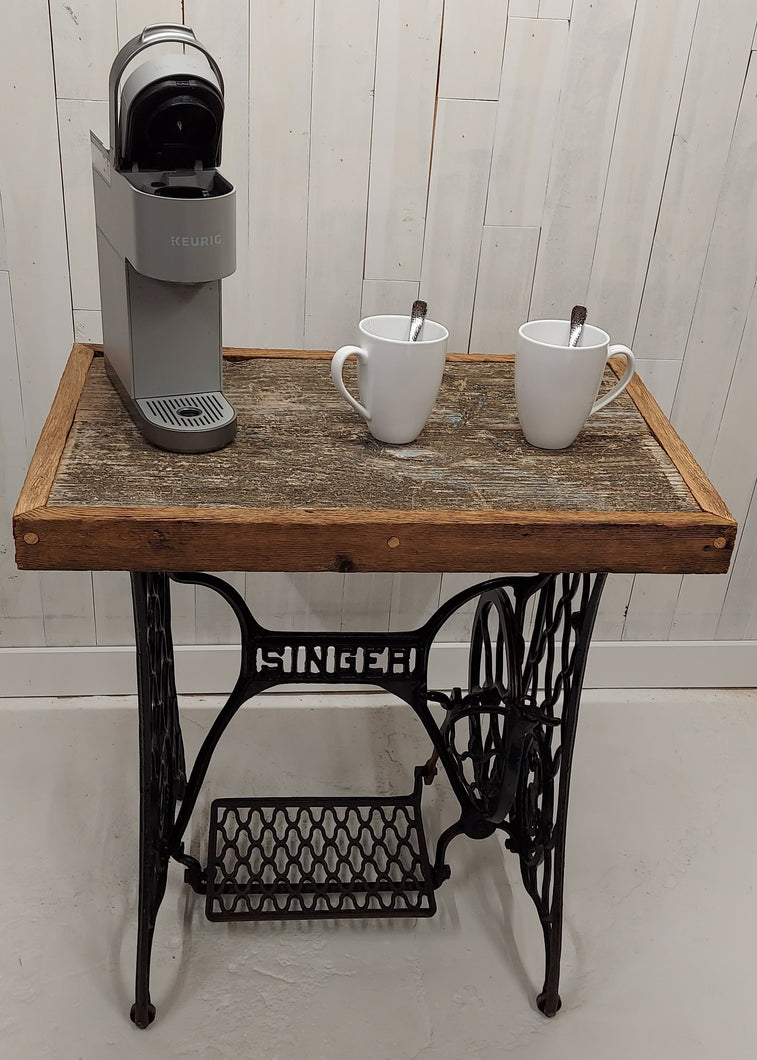 A barnboard tabletop affixed to a Singer sewing machine stand.  Displays a Keurig coffee maker and two coffee cups.