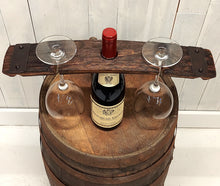 Load image into Gallery viewer, A top view of a wine bottle centered on a wooden barrel top, with a rustic barrel stave set over the bottle neck, and a stemmed wine glass hanging on each side of the bottle.

